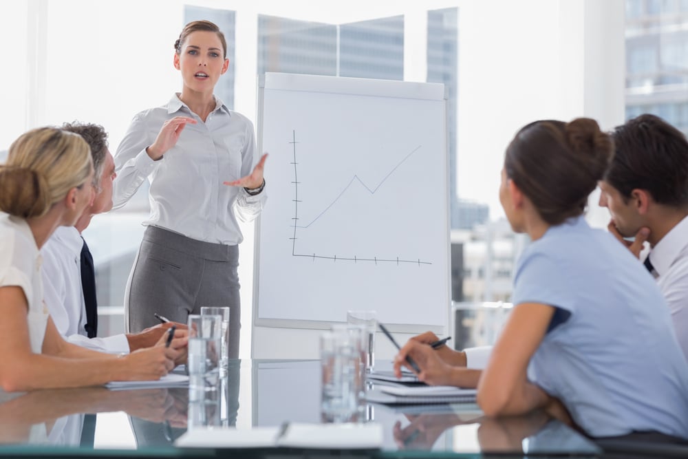 Businesswoman giving explication in front of a growing chart on a whiteboard during a meeting Businesswoman giving explication in front of a growing chart on a whiteboard during a meeting