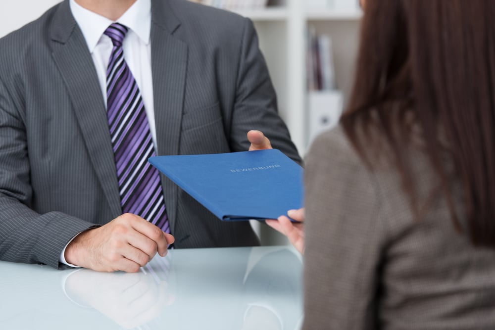 Employment interview with a close up view of a female applicant handing over a file containing her curriculum vitae to the businessman conducting the interview Employment interview with a close up view of a female applicant handing over a file containing her curriculum vitae to the businessman conducting the interview